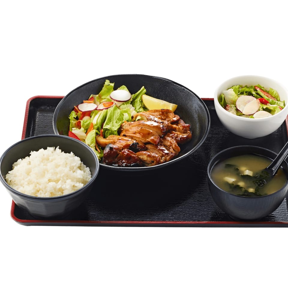 Teriyaki chicken with salad, rice, and miso soup on a black tray.