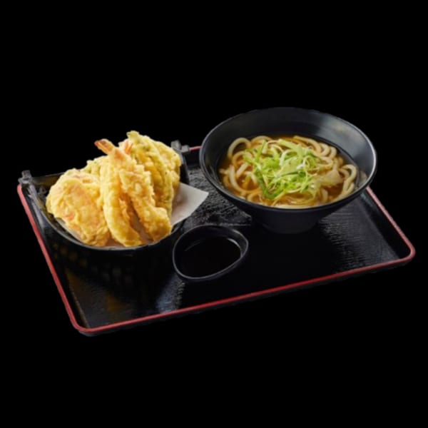 Tempura shrimp and vegetables with a bowl of udon noodles and a small dish of sauce on a black tray.