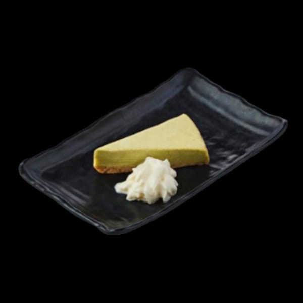 A slice of green tea cheesecake with a dollop of whipped cream on a black rectangular plate.